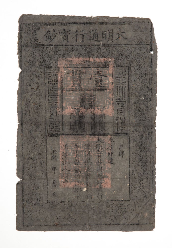 Item ID: 8126 Woodblock banknote (337 x 220 mm.), printed on blueish slate-colored mulberry bark paper, with six-character inscription at top giving name of banknote: Da Ming tongxing baochao [Great Ming Circulating Treasure Certificate], with a woodcut border of dragons & traces of three official seals in red. [China]: “1375”-1425. MING BANKNOTE: DA MING BAOCHAO.