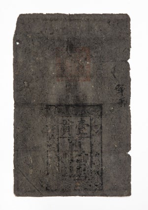 Woodblock banknote (337 x 220 mm.), printed on blueish slate-colored mulberry bark paper, with six-character inscription at top giving name of banknote: Da Ming tongxing baochao [Great Ming Circulating Treasure Certificate], with a woodcut border of dragons & traces of three official seals in red. [China]: “1375”-1425.